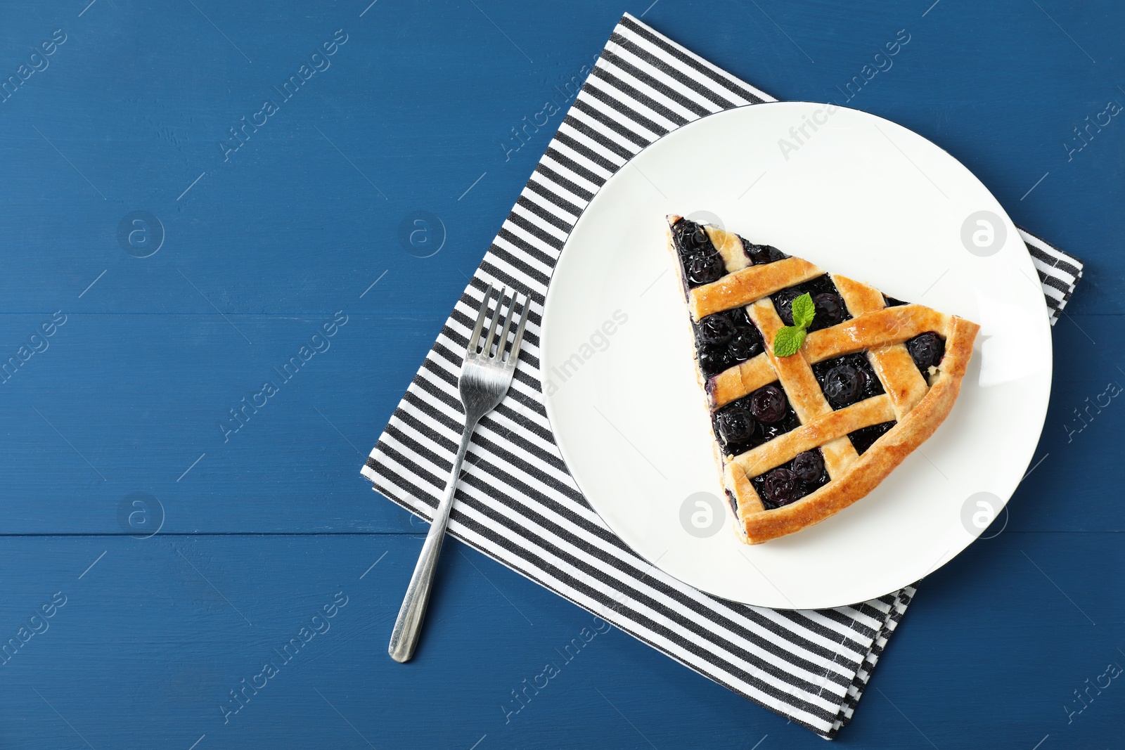 Photo of Piece of tasty homemade pie with blueberries served on blue wooden table, flat lay. Space for text