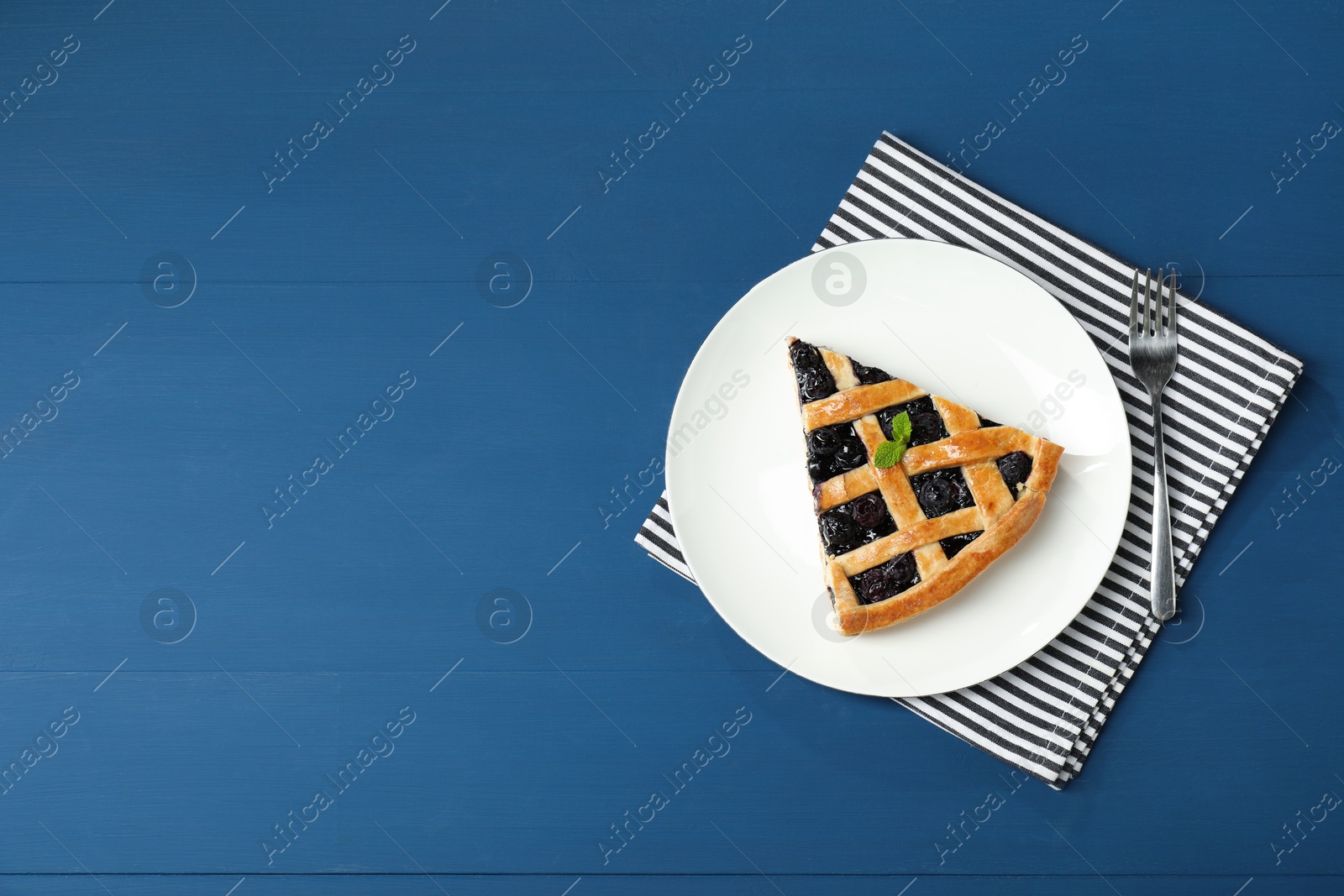 Photo of Piece of tasty homemade pie with blueberries served on blue wooden table, flat lay. Space for text