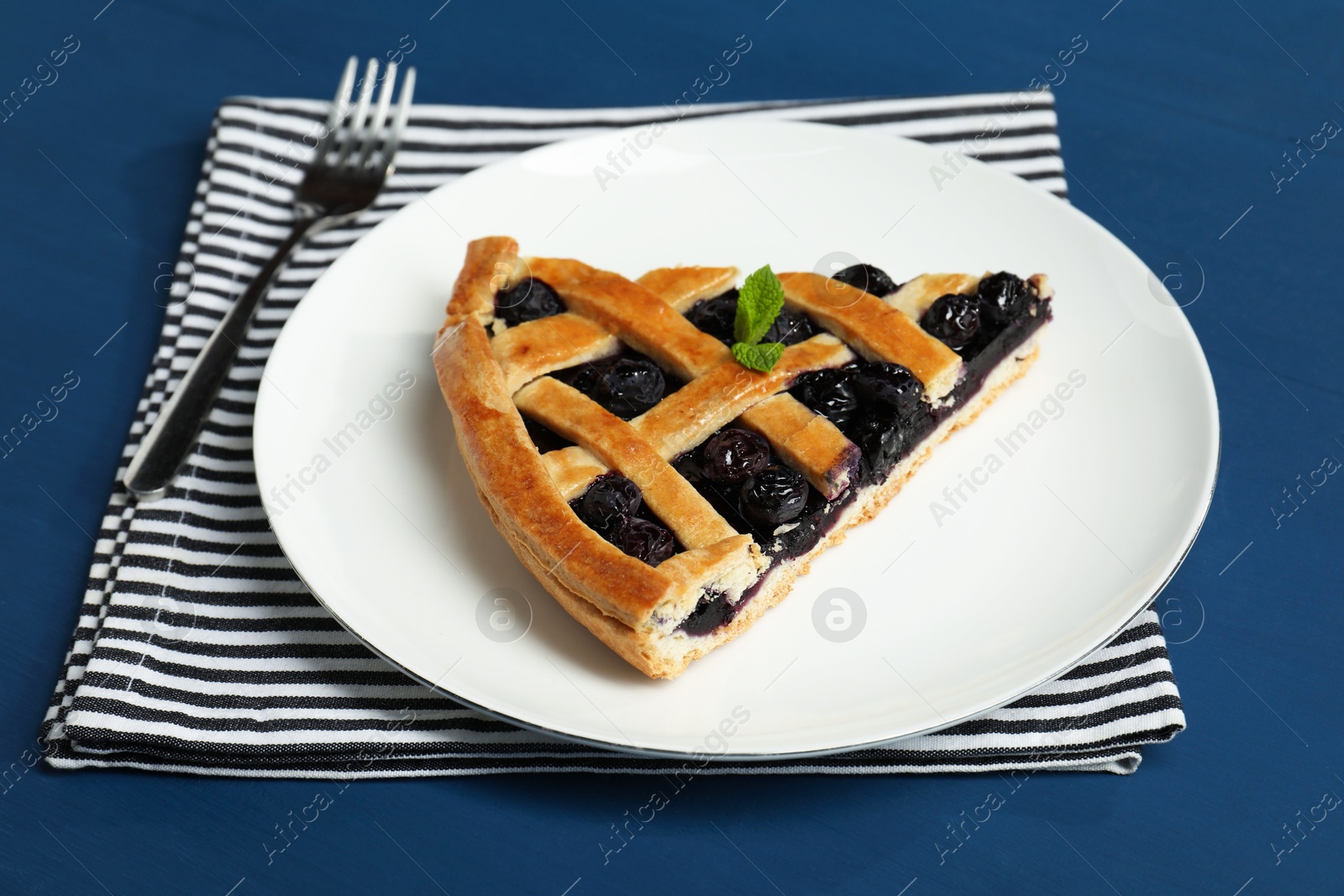 Photo of Piece of tasty homemade pie with blueberries served on blue table