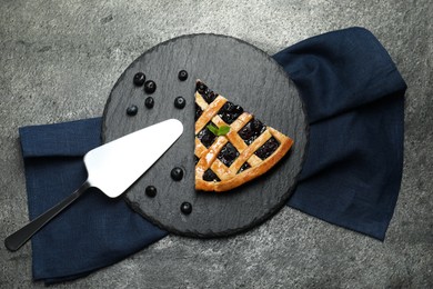 Photo of Piece of tasty homemade pie with blueberries and server on grey textured table, flat lay