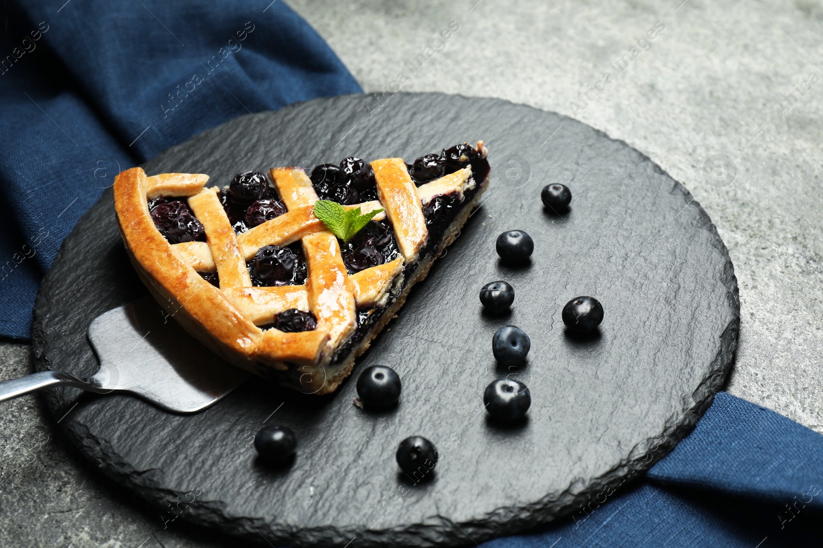 Photo of Piece of tasty homemade pie with blueberries and server on grey table