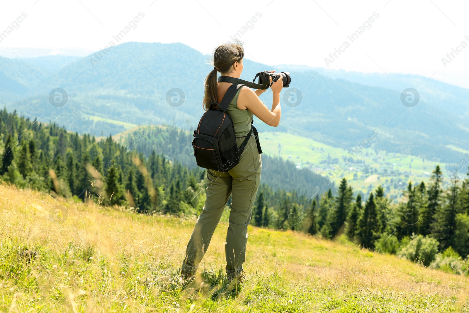 Photo of Photographer with backpack and camera taking picture of beautiful mountains, back view