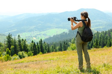 Photographer with backpack and camera taking picture of beautiful mountains, back view. Space for text