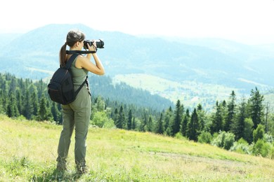 Photographer with backpack and camera taking picture of beautiful mountains, back view. Space for text