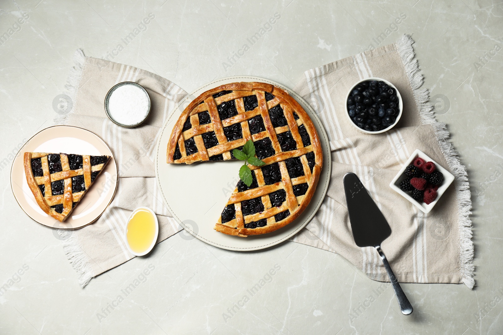 Photo of Tasty homemade pie with blueberries, fresh berries honey and cake server on gray textured table, flat lay