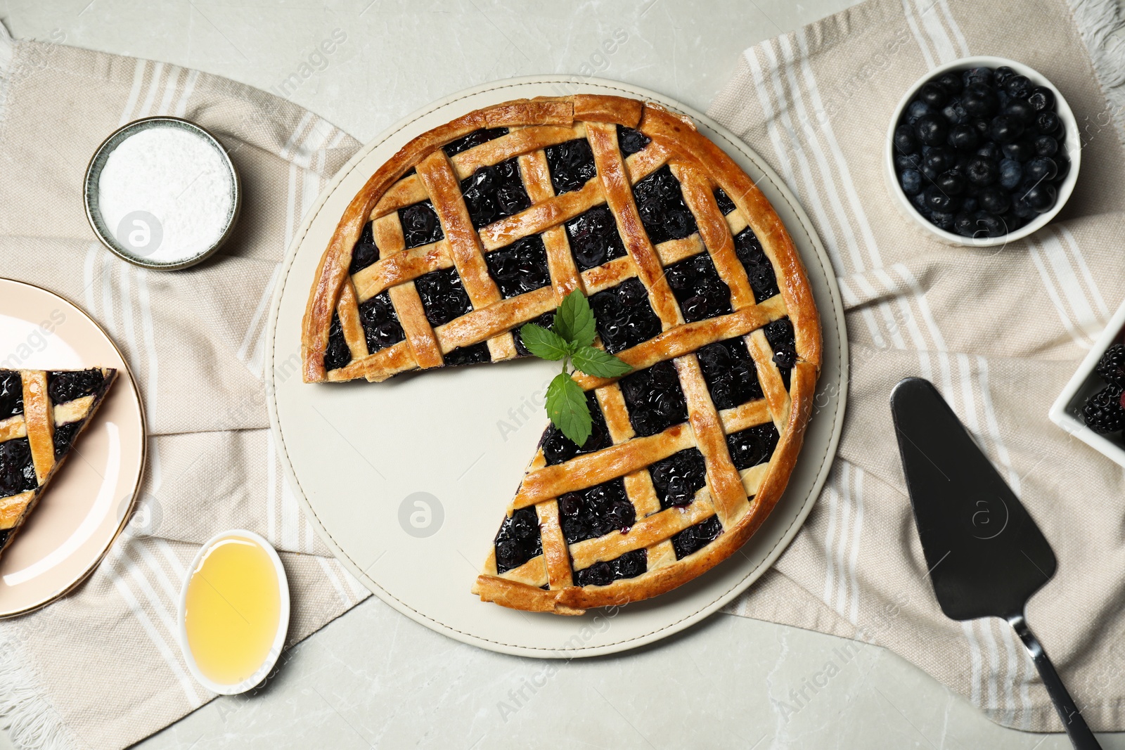 Photo of Tasty homemade pie with blueberries, honey and cake server on gray textured table, flat lay