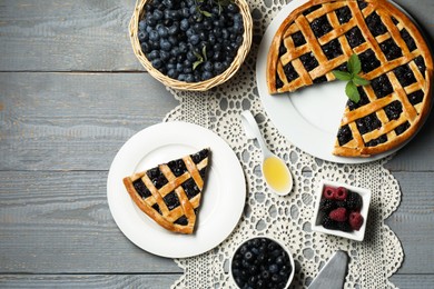 Photo of Tasty homemade pie with blueberries, fresh berries honey and cake server on gray wooden table, flat lay