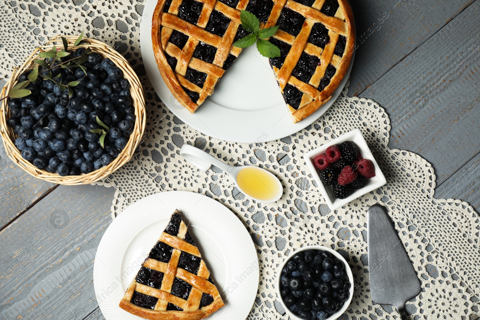 Photo of Tasty homemade pie with blueberries, fresh berries honey and cake server on gray wooden table, flat lay