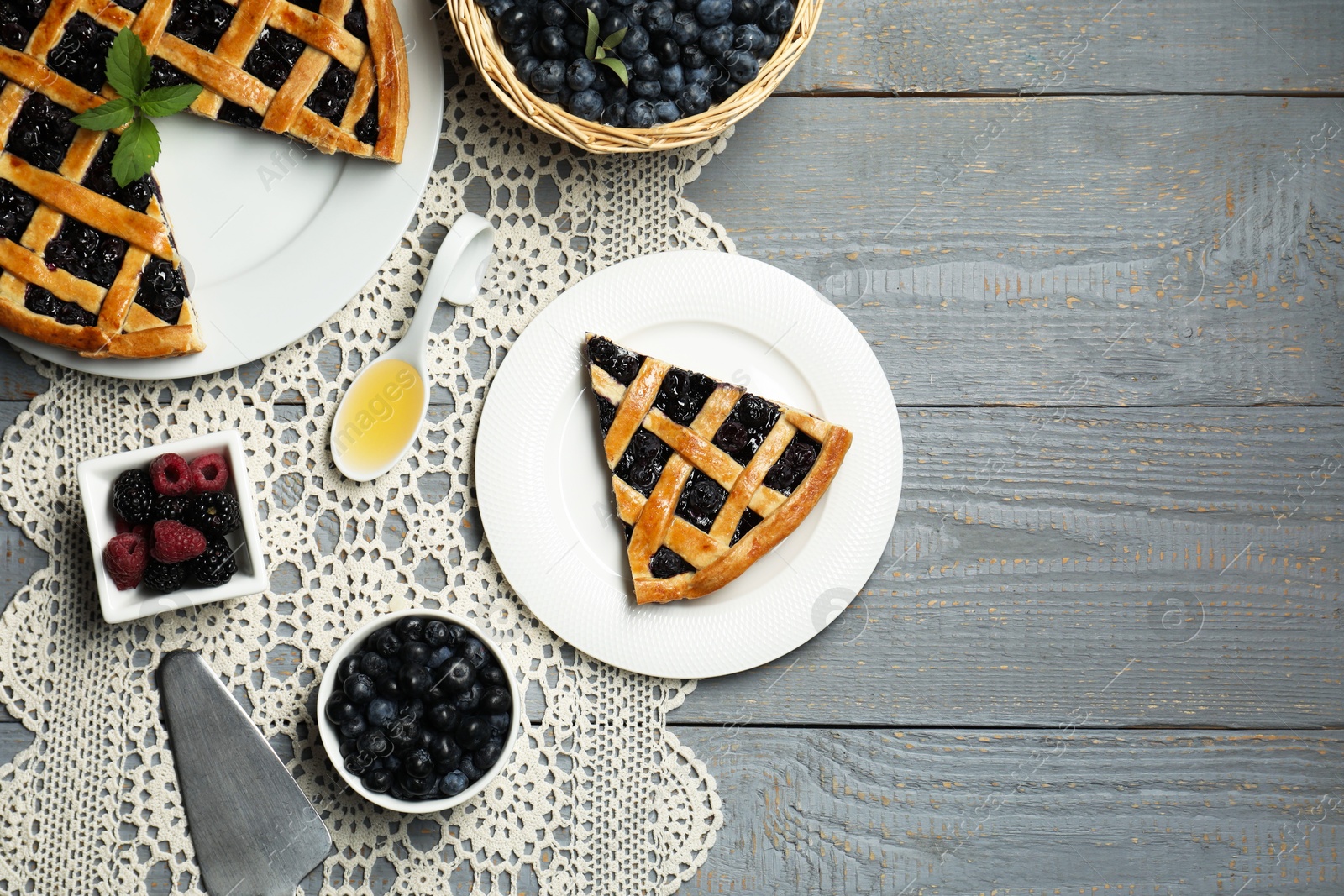 Photo of Tasty homemade pie with blueberries, fresh berries honey and cake server on gray wooden table, flat lay. Space for text