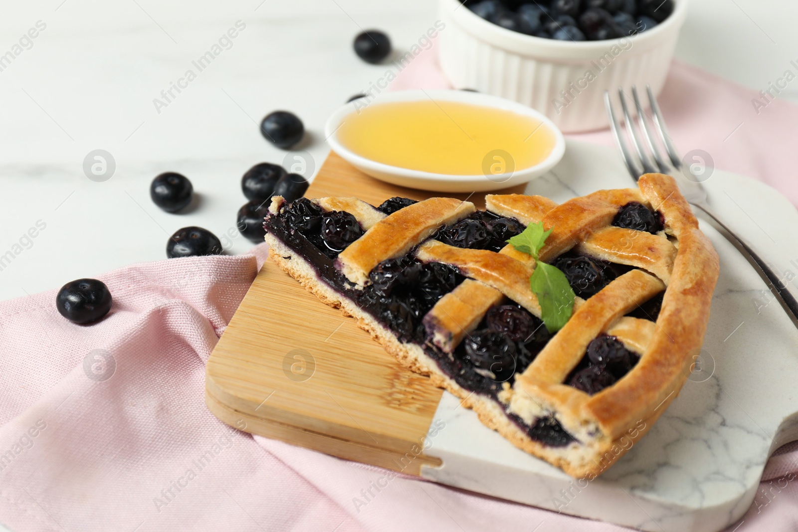 Photo of Piece of tasty homemade pie with blueberries and honey on white table, closeup