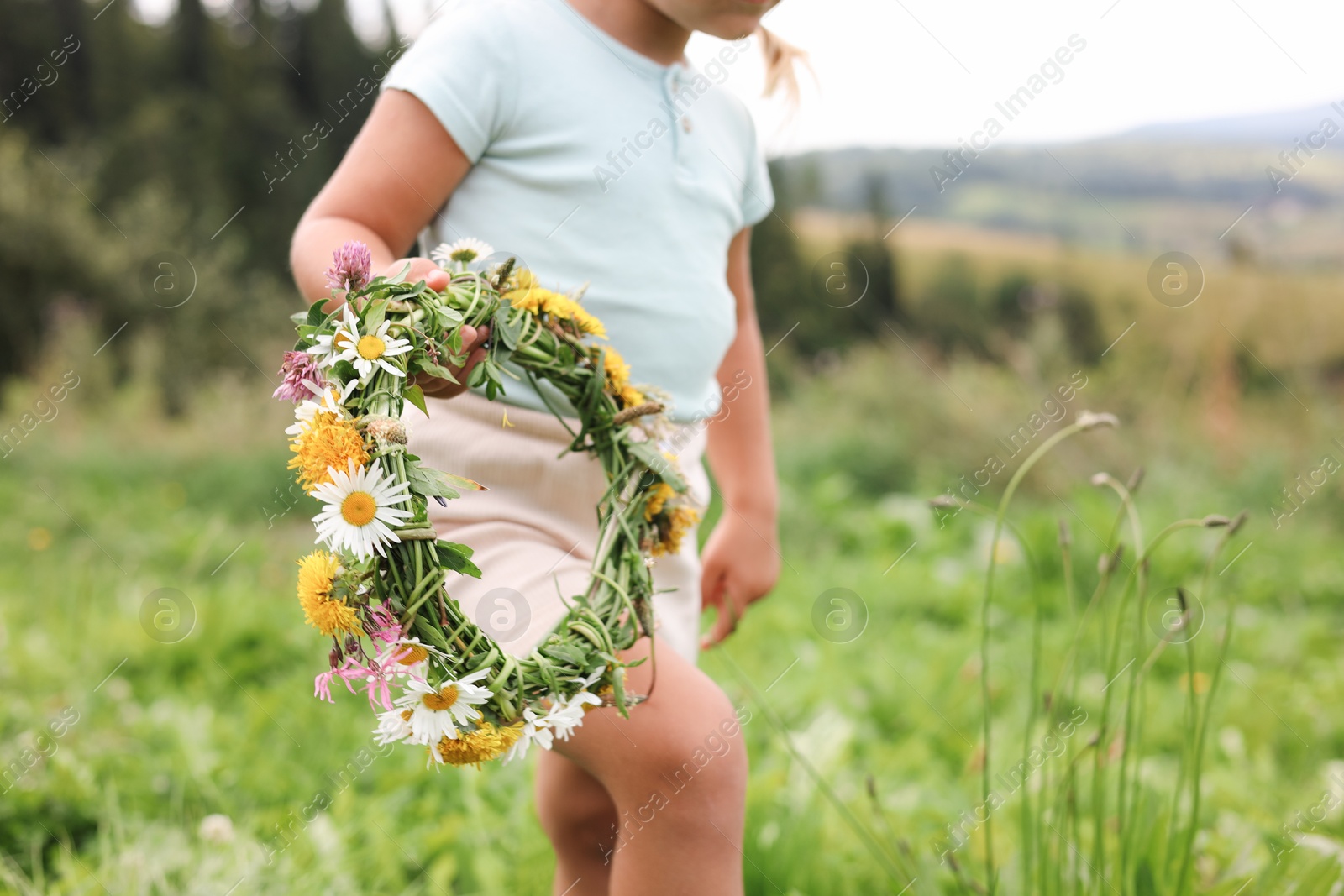 Photo of Little girl with floral wreath walking at meadow, closeup. Child enjoying beautiful nature