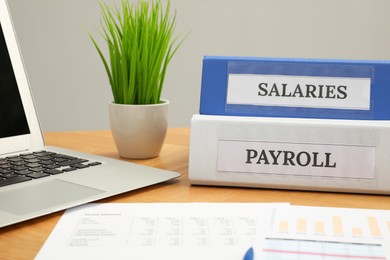 Photo of Payroll. Folders, charts and laptop on wooden table, closeup