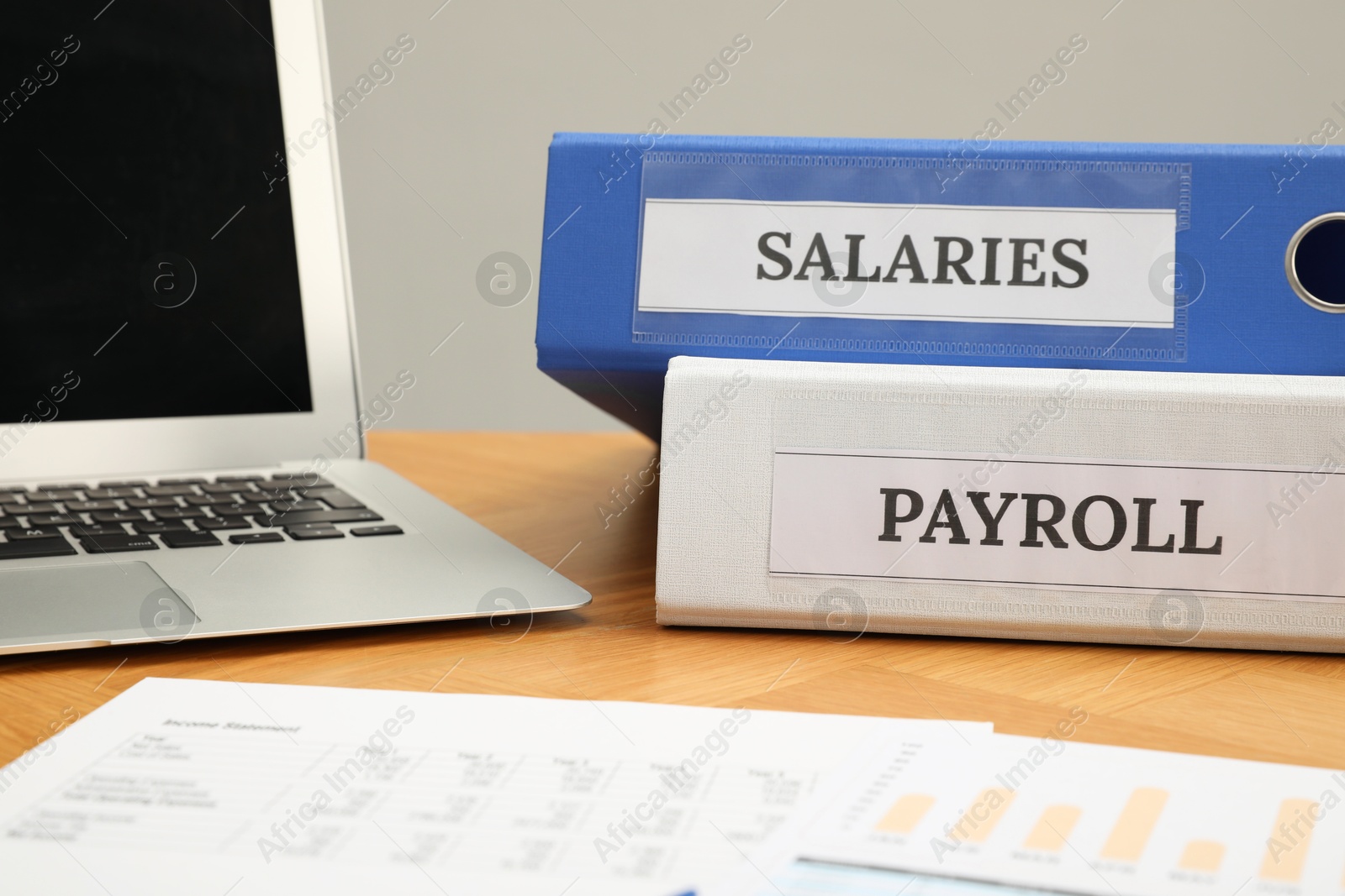 Photo of Payroll. Folders, charts and laptop on wooden table, closeup