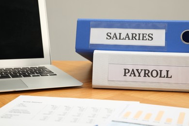 Photo of Payroll. Folders, charts and laptop on wooden table, closeup