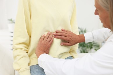 Doctor examining woman with stomach pain in clinic, closeup