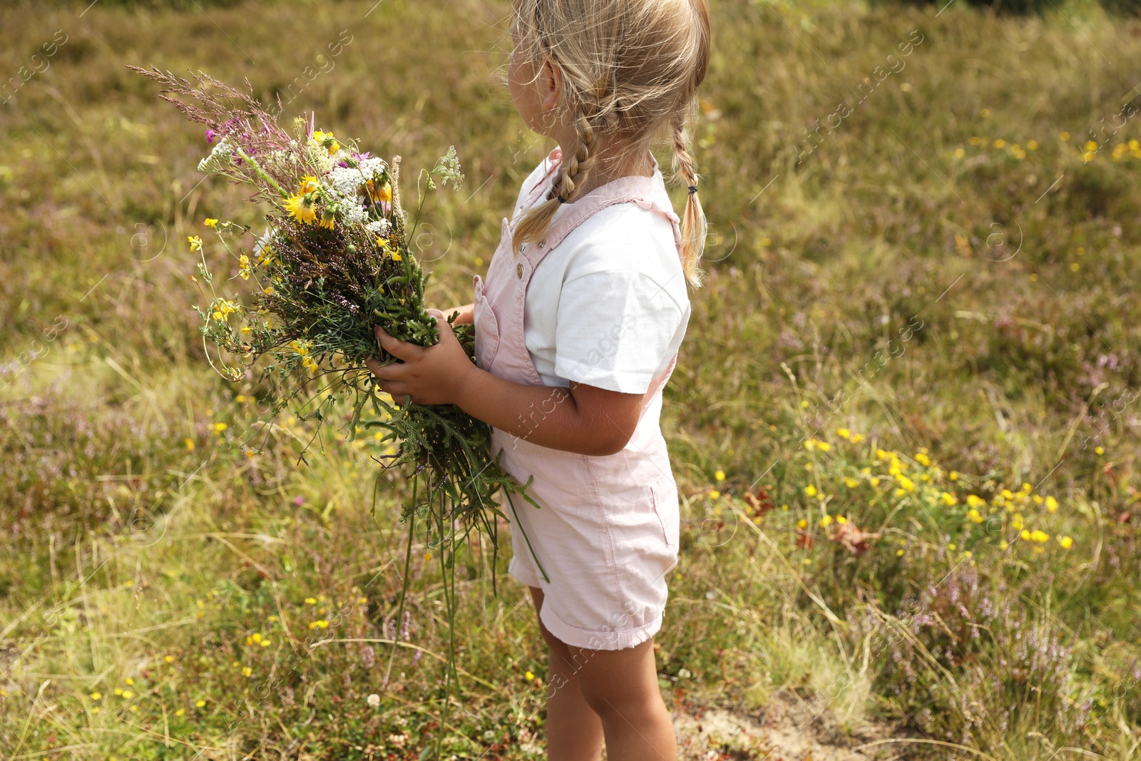 Photo of Little girl with bouquet of wildflowers at field. Child enjoying beautiful nature