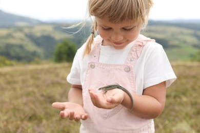 Cute little girl holding lizard at field. Child enjoying beautiful nature