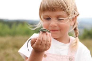 Photo of Little girl exploring lizard on blurred background. Child enjoying beautiful nature