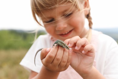 Photo of Smiling little girl exploring lizard on blurred background. Child enjoying beautiful nature