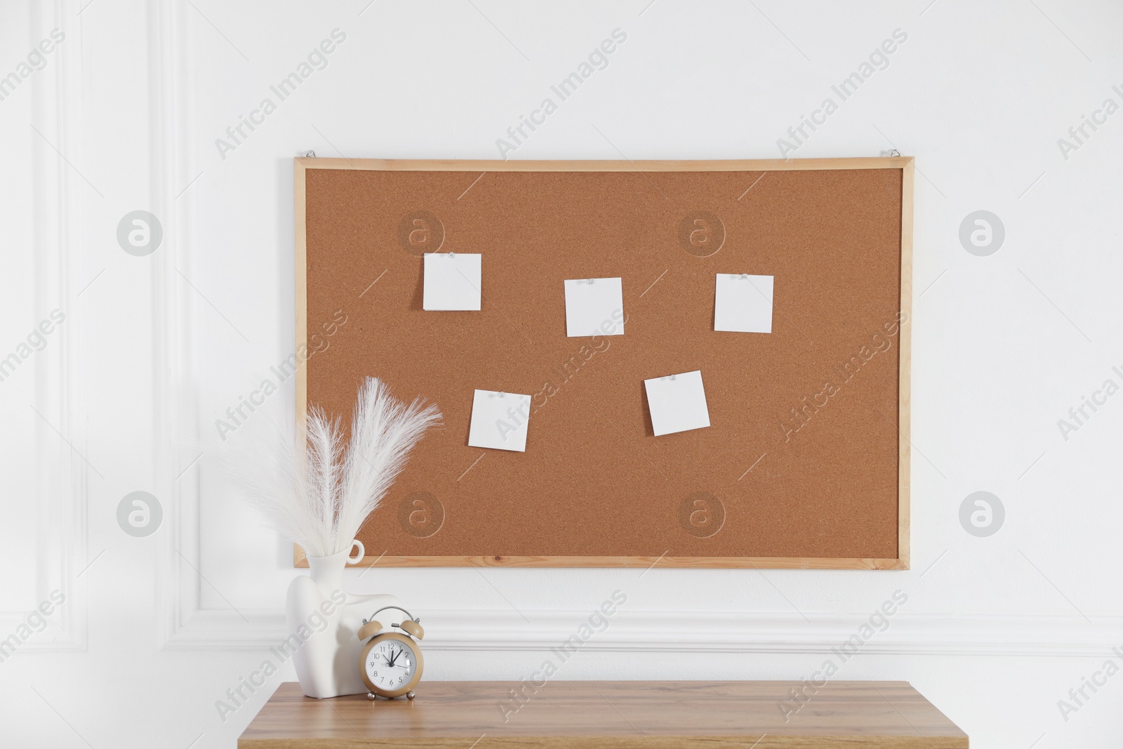 Photo of Cork board with blank paper notes, alarm clock and decorative branches in vase on wooden table