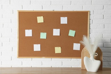 Photo of Cork board with blank paper notes and decorative elements on wooden table near white brick wall