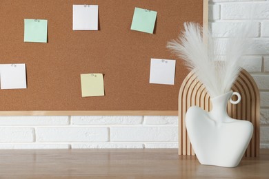 Photo of Cork board with blank paper notes and decorative elements on wooden table near white brick wall