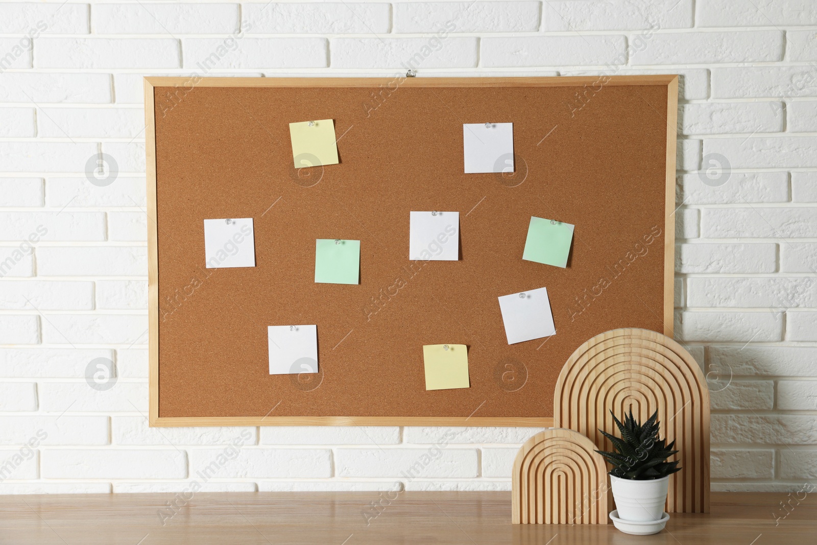 Photo of Cork board with blank paper notes and decorative elements on wooden table near white brick wall