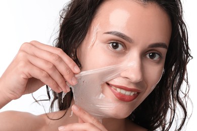 Smiling woman peeling off face mask on white background, closeup