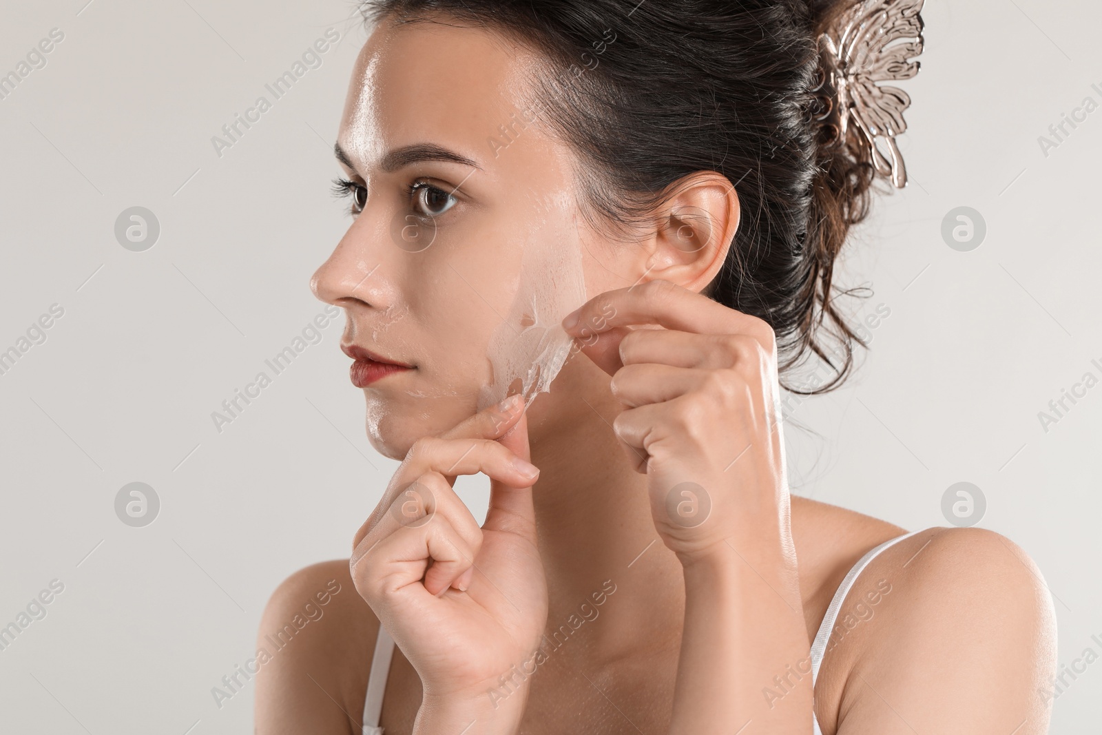 Photo of Beautiful woman peeling off face mask on light grey background