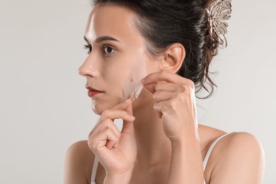 Beautiful woman peeling off face mask on light grey background