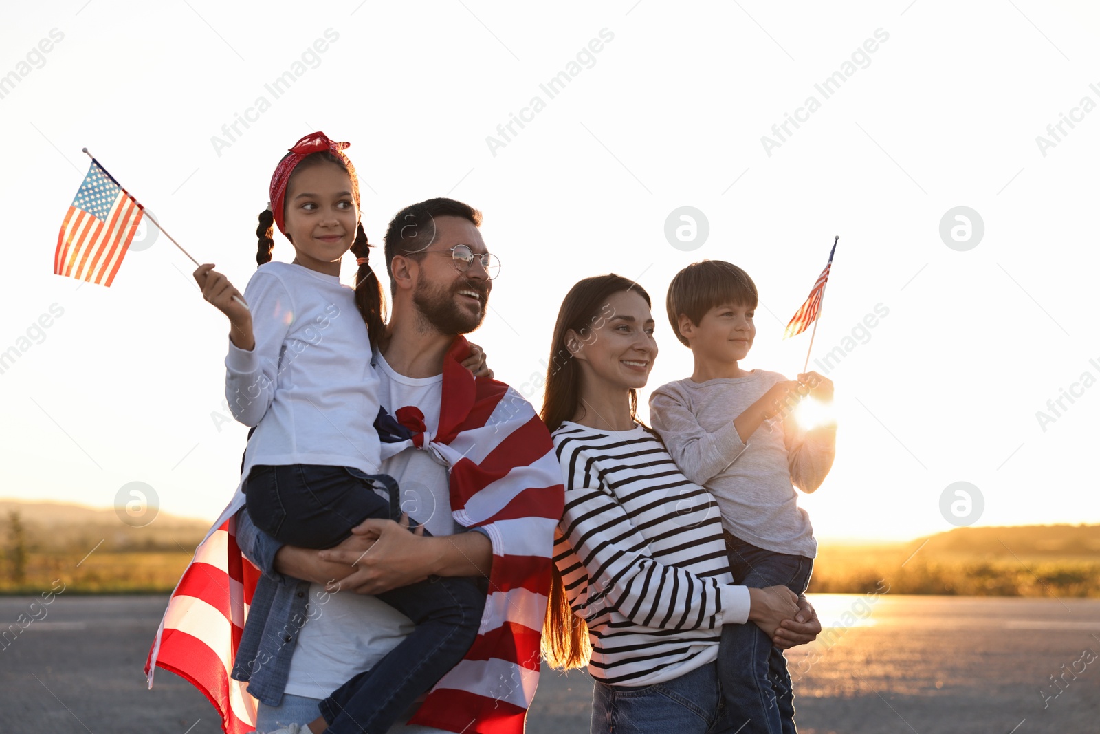 Photo of Family portrait of happy parents with children waving USA flags outdoors