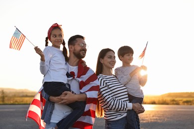 Family portrait of happy parents with children waving USA flags outdoors