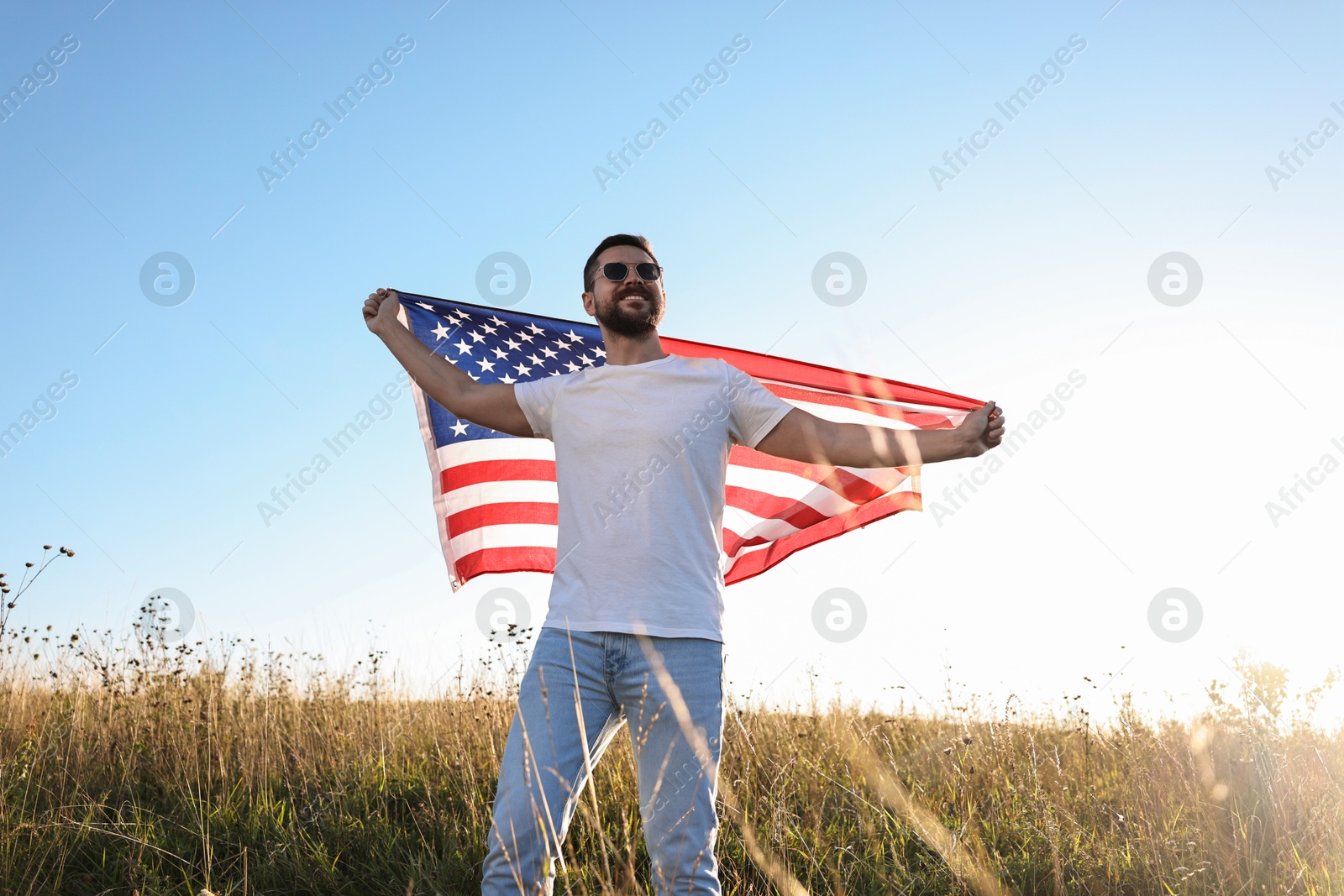 Photo of Happy man with flag of USA outdoors, low angle view