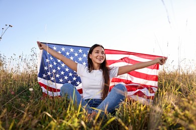 Photo of Happy woman with flag of USA sitting on grass outdoors