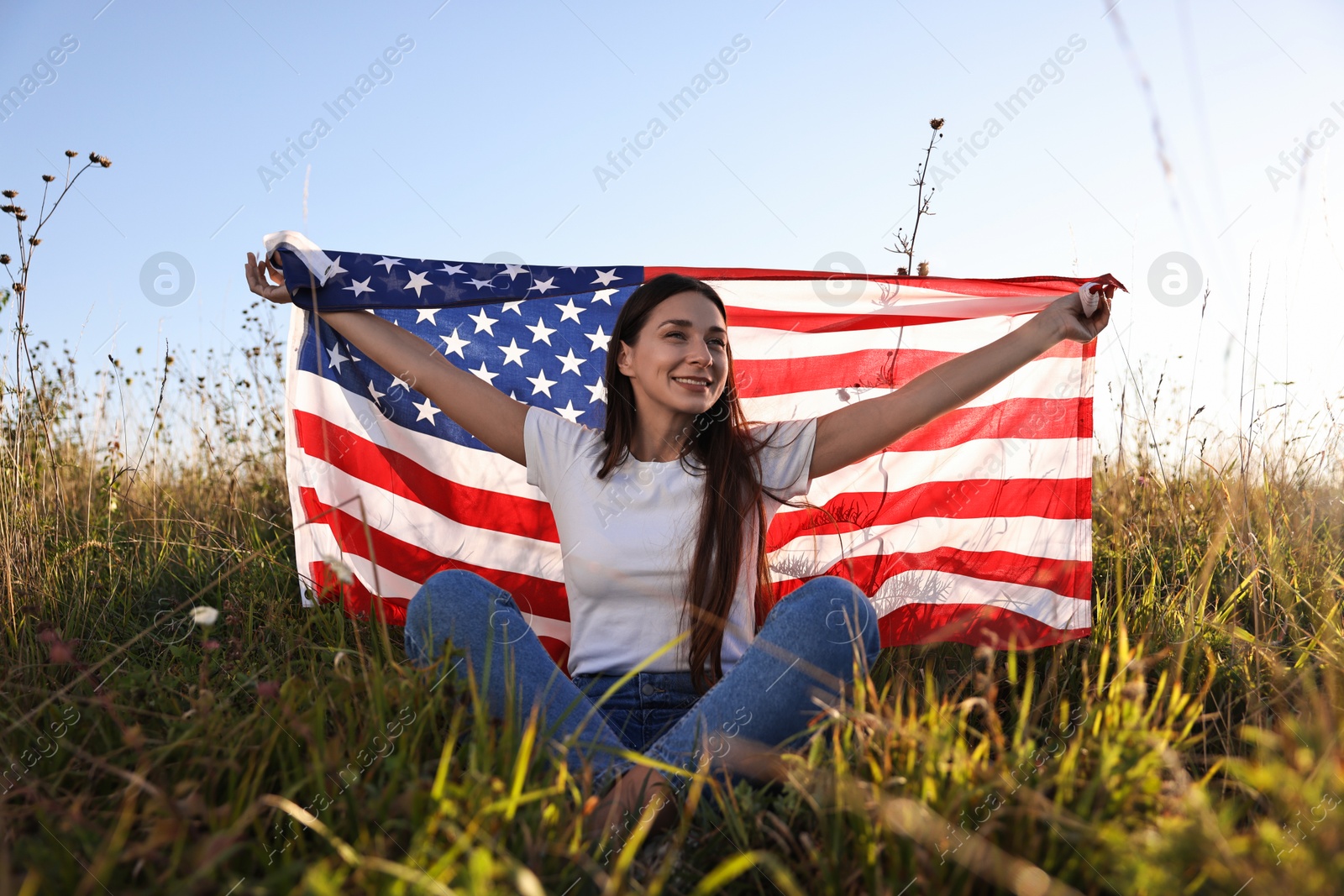 Photo of Happy woman with flag of USA sitting on grass outdoors