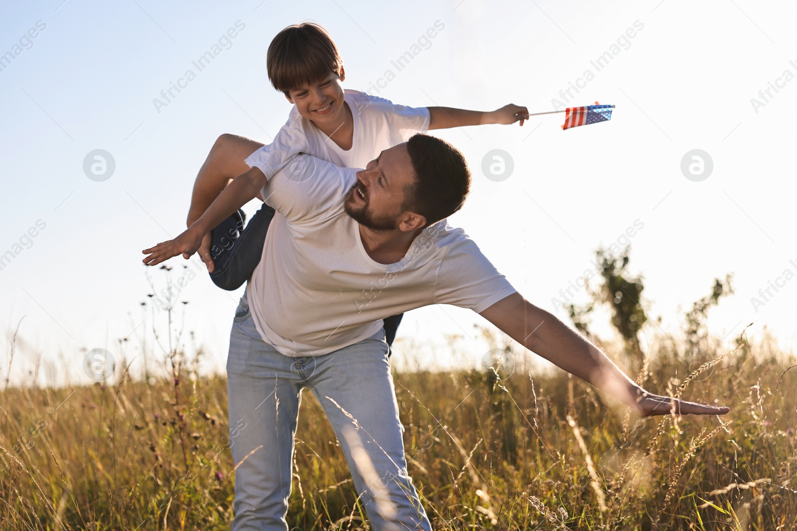 Photo of Happy father and son with flag of USA having fun outdoors