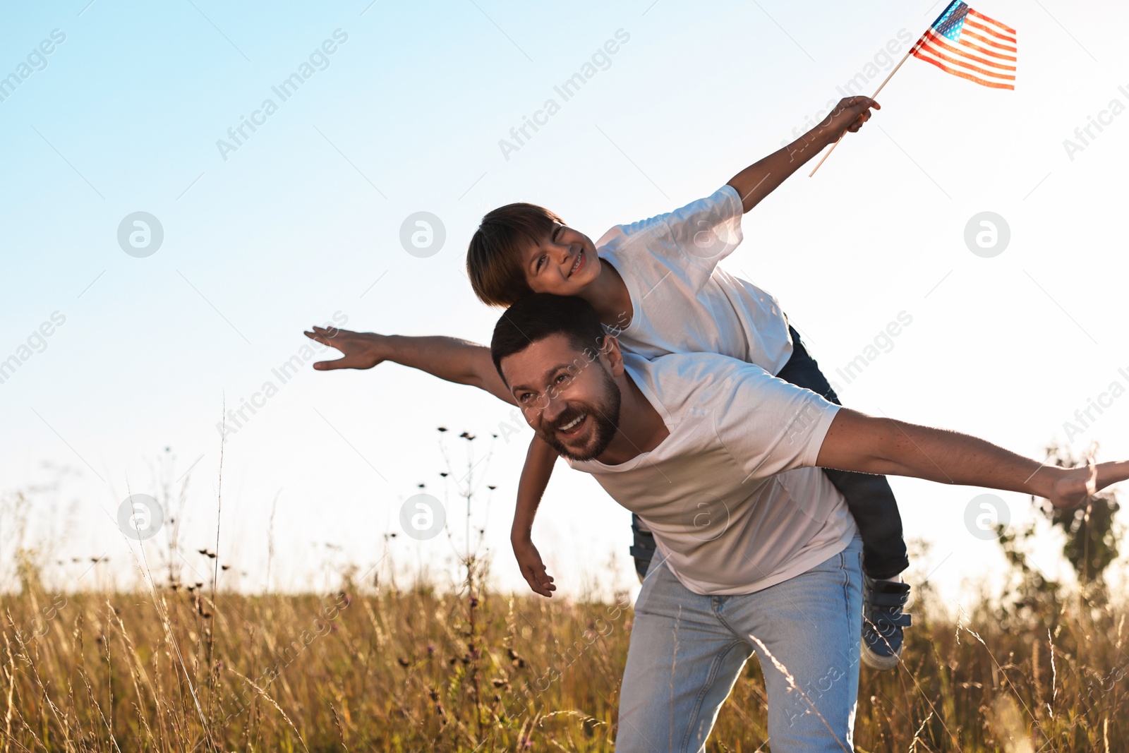 Photo of Happy father and son with flag of USA having fun outdoors. Space for text