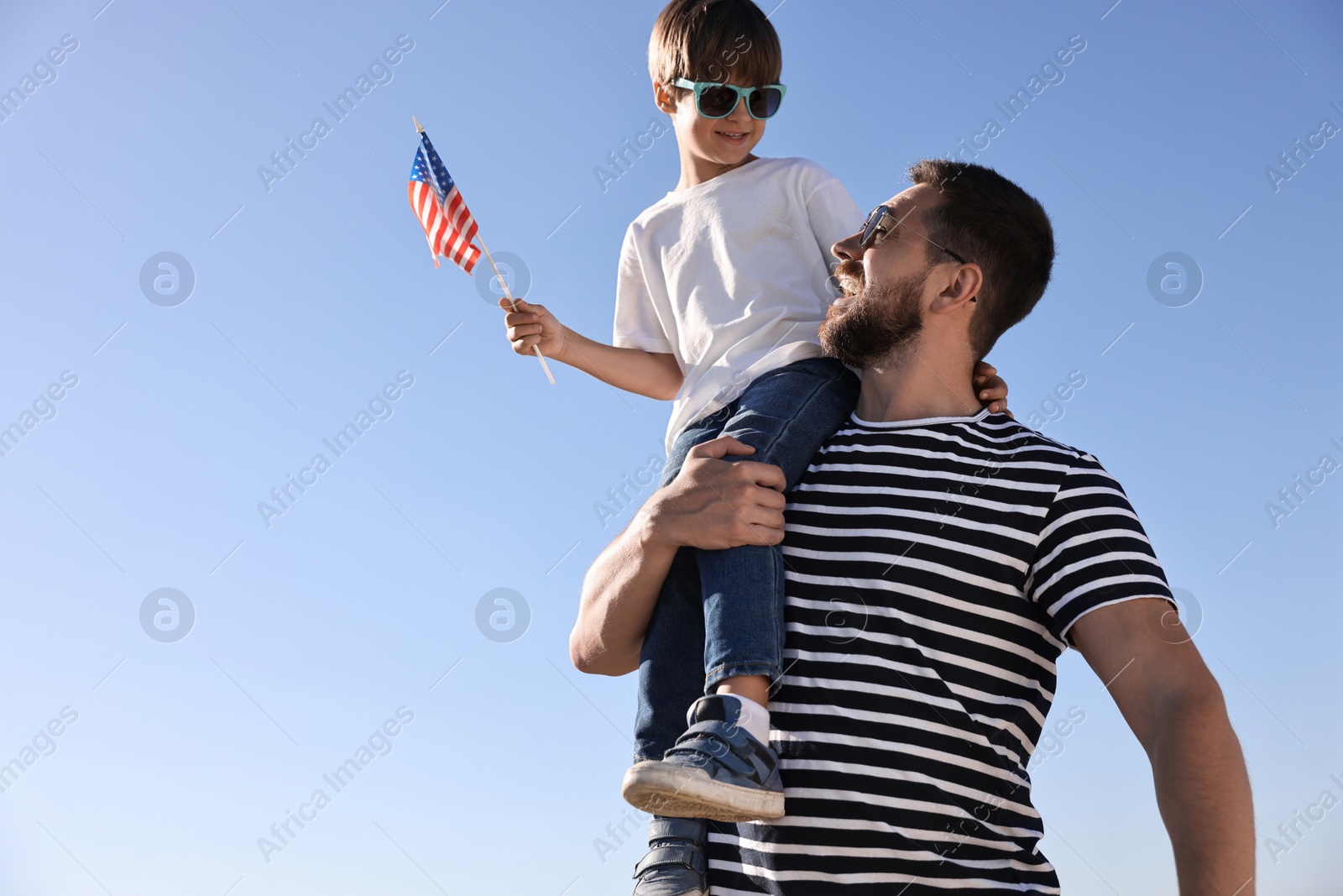 Photo of Happy father and son with flag of USA outdoors, low angle view. Space for text