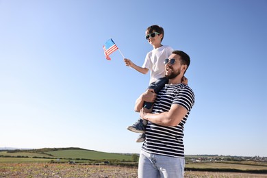 Happy father and son with flag of USA outdoors. Space for text