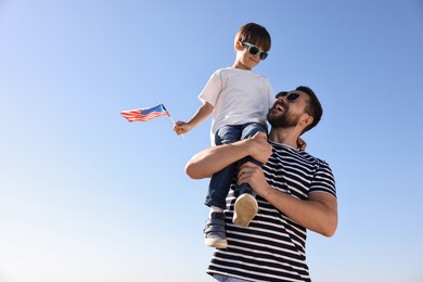 Photo of Happy father and son with flag of USA outdoors, low angle view. Space for text