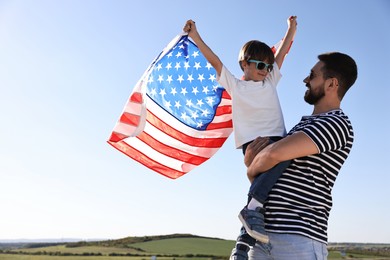 Happy father and son with flag of USA outdoors. Space for text