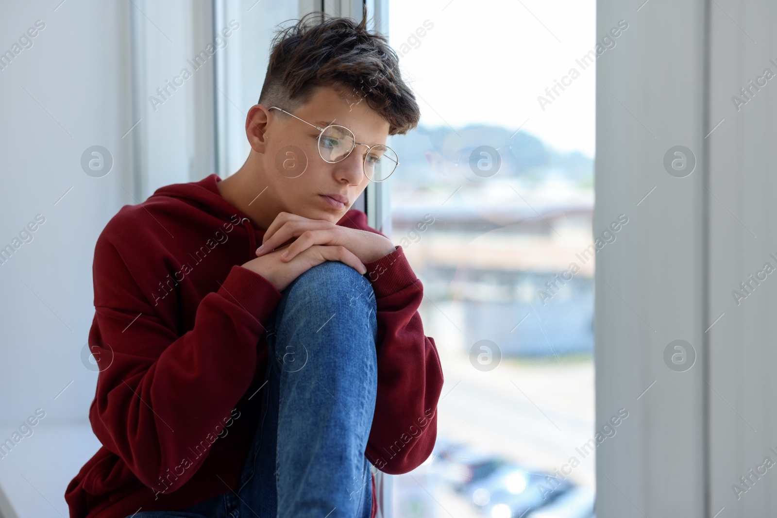 Photo of Loneliness concept. Sad teenage boy near window indoors, space for text