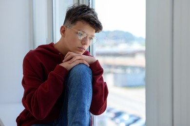 Loneliness concept. Sad teenage boy near window indoors, space for text