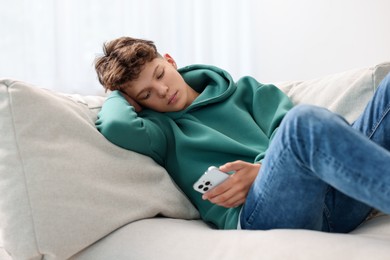 Loneliness concept. Sad teenage boy using smartphone on sofa at home