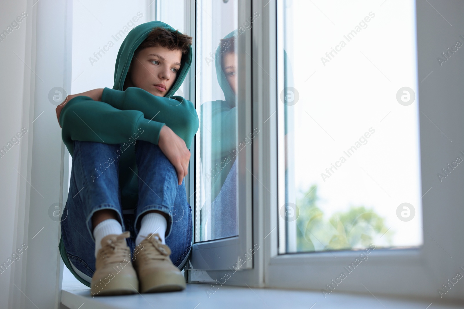 Photo of Loneliness concept. Sad teenage boy on windowsill indoors