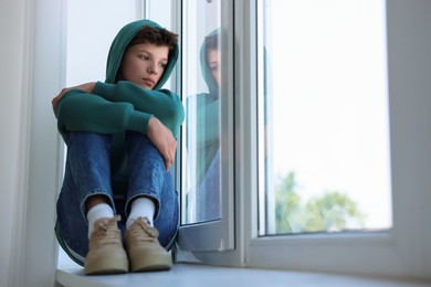 Photo of Loneliness concept. Sad teenage boy on windowsill indoors