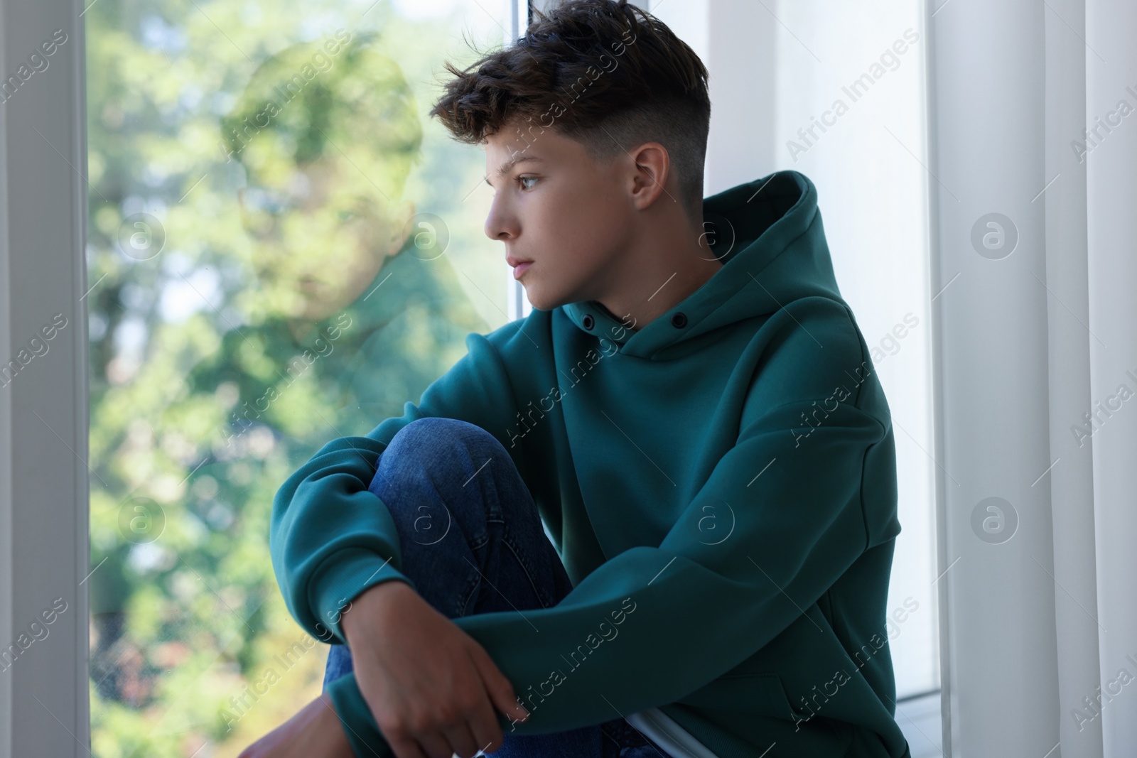 Photo of Loneliness concept. Sad teenage boy near window indoors