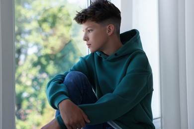 Photo of Loneliness concept. Sad teenage boy near window indoors