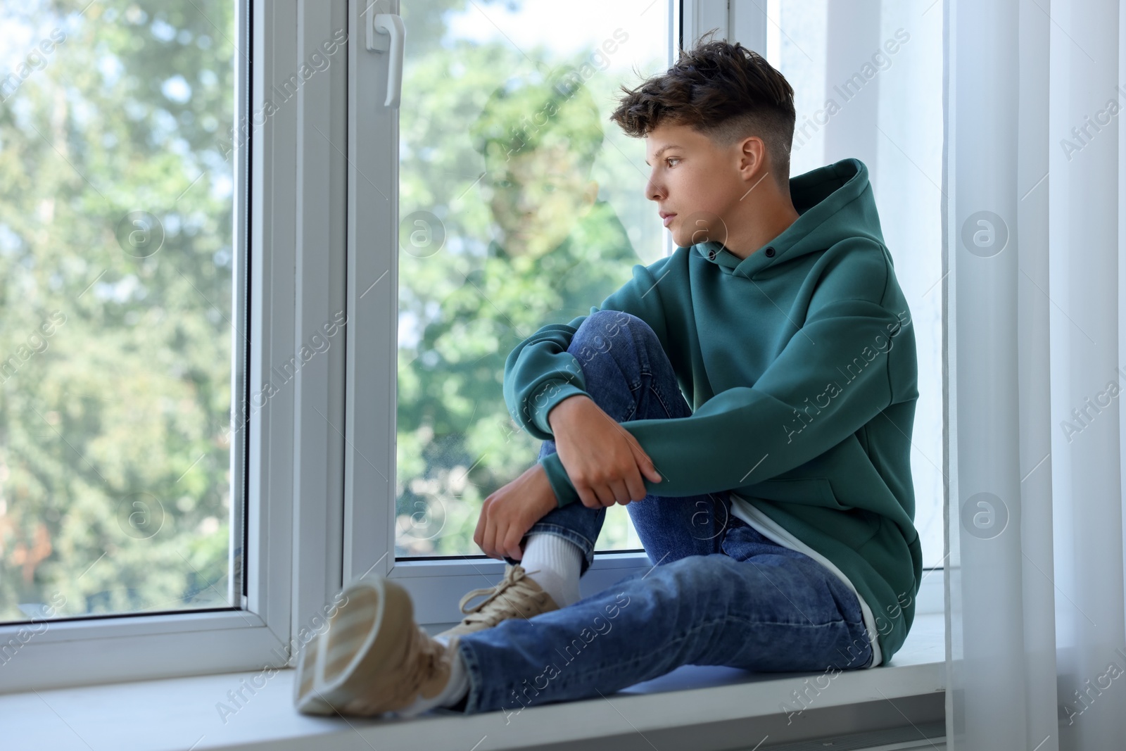 Photo of Loneliness concept. Sad teenage boy on windowsill indoors