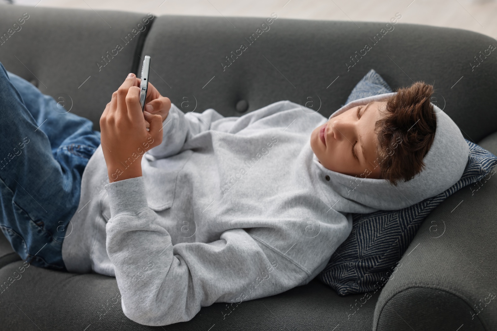 Photo of Loneliness concept. Sad teenage boy using smartphone on sofa at home